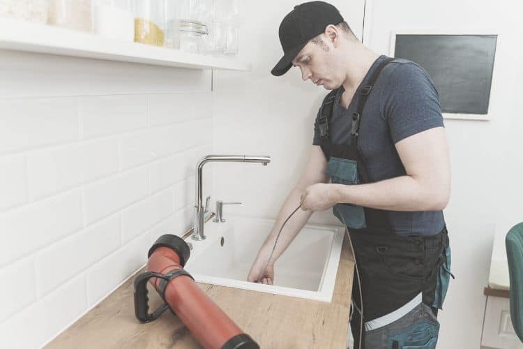 plumber using plumbing snake to clear a sink clog