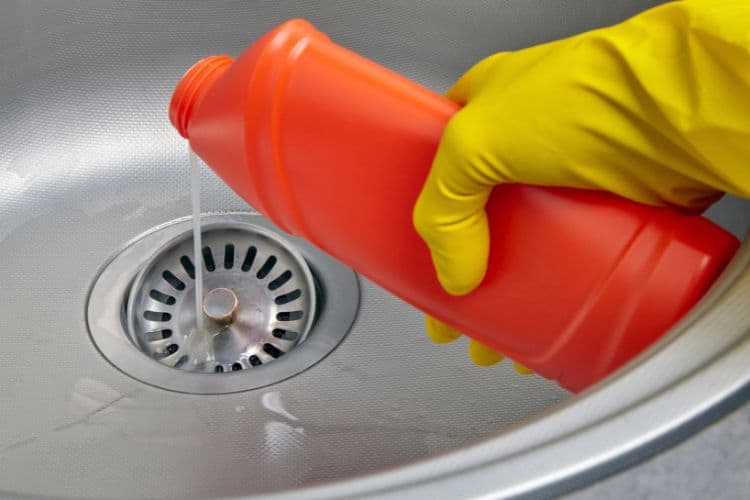 Gloved hand pouring chemical drain cleaner down the sink