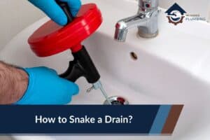 How to Snake a Drain - No Hassle Plumbing.com Featured image showing a drain auger sitting in a clogged bathroom sink with hair clogs stuck to the auger tip
